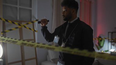 Rozetli Afrikalı Amerikalı bir dedektif el feneri kullanarak bir suç mahallini araştırıyor.