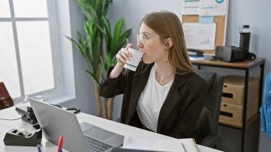 Genç profesyonel bir kadın, tipik bir iş günü atmosferini yansıtan modern ofisinde kahve molası veriyor.