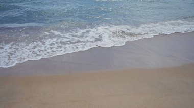 Yumuşak dalgalar güneşli bir sahil gününde kumlu sahilde sükuneti ve doğal güzelliği tasvir eder..