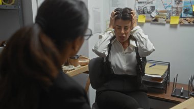 Bir ofiste iki kadın dedektif, biri sıkıntılı, diğeri de dinliyor, soruşturma kanıtıyla çevrili..