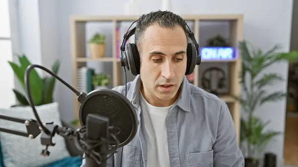 stock image Hispanic man speaking into microphone in a radio studio with headphones and on-air sign.