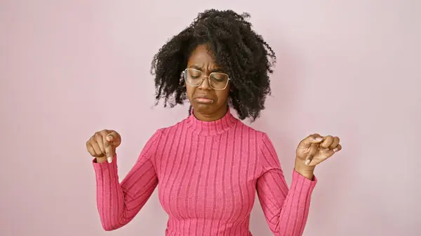 stock image A young black woman in a pink sweater showing thumbs down in a pink-hued room