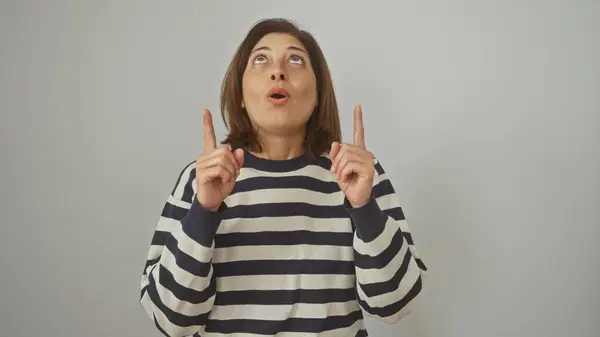 stock image A middle-aged hispanic woman in a striped sweater gestures upward against a white background, expressing surprise or curiosity.