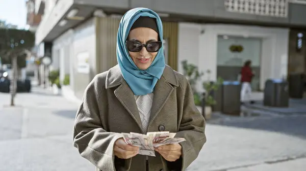 stock image Middle-aged woman in hijab counts saudi riyals on urban street