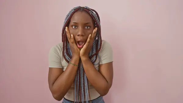 stock image Portrait of a surprised african woman with braids against a pink background.