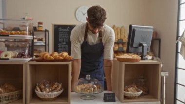 Fırında çalışan genç bir adam. Tezgahın arkasında duruyor. Kollarını kavuşturup gülümsüyor.