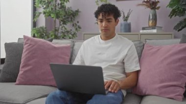 İspanyol adam modern oturma odasında dizüstü bilgisayarla hayal kırıklığına uğradı.