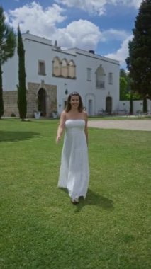 Beyaz elbiseli genç bir kadın İtalya, Puglia 'da güzel bir villanın önünde yürüyor, açık mavi bir gökyüzünün altında, sakin bir ortamda Avrupa cazibesi ve zarafetini sergiliyor..