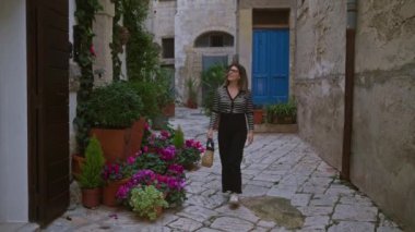 Genç bir İspanyol kadın polignano 'nun pitoresk caddelerinde yürüyor Puglia, İtalya' da canlı çiçekler ve kırsal mimariyle çevrili bir kısrak..