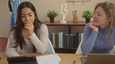 Modern bir ofis ortamında dizüstü bilgisayar ve tabletle birlikte çalışan iki kadın..