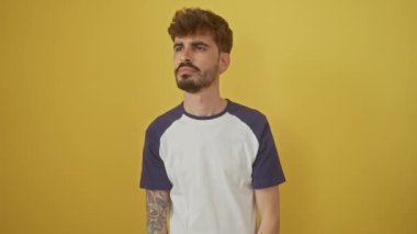 Gülümseyen İspanyol genç adam uzaklara bakıyor, izole edilmiş sarı arka planda duruyor, el ele tutuşmuş.