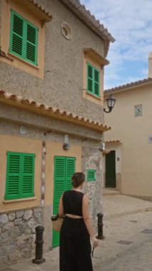 İspanyol kadın siyah elbiseli açık havada liman de valldemossa, mallorca, İspanya 'da geleneksel taş evler ve parlak yeşil panjurlarla yürüyor.