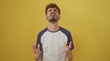 Genç, agresif İspanyol bir adam, sinirden delicesine bağırıyor. Parlak sarı bir arka planda izole bir şekilde duruyor. Öfke ve stresi çılgınca bağırıp çağırarak ifade ediyor.