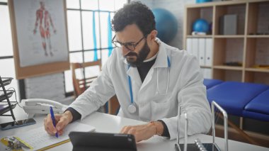 Sakallı bir erkek doktor hastane odasına not yazıyor. Yaşı, deneyimi ve sağlık sektöründeki profesyonelliği özetliyor..