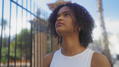 Kıvırcık saçlı genç Afrikalı Amerikalı kadın gündüz vakti şehir sokağına bakıyor..