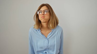 Yanaklarını şişirirken komik bir yüz ifadesi takınan genç sarışın kadın beyaz bir duvar arkasında izole edilmiş.