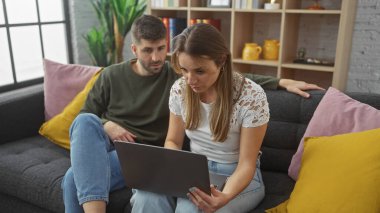 Bir kadın ve bir erkek, rahat bir oturma odasındaki kanepeye oturup dikkatle dizüstü bilgisayarın ekranına bakıyorlar..