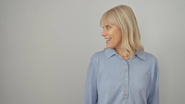 Beyaz bir arka planda günlük mavi elbiseli gülümseyen sarışın bir kadının yan görünüm portresi.