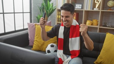 Samimi bir oturma odasında spor izlerken sakallı heyecanlı genç adam tezahürat yapıyor..