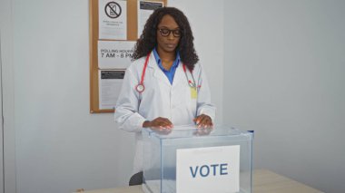 Kıvırcık saçlı, doktor önlüğü giymiş yetişkin bir Afro-Amerikalı kadın oy pusulasını kapalı bir yerde kullanıyor..