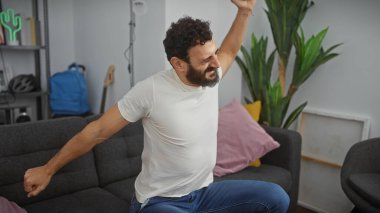 Sakallı, orta yaşlı bir adam, rahat, modern bir oturma odasında rahatça uzanıyor..