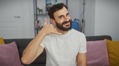 Sakallı, yakışıklı, orta yaşlı bir adam. Oturma odasında bana jest yapıyor..