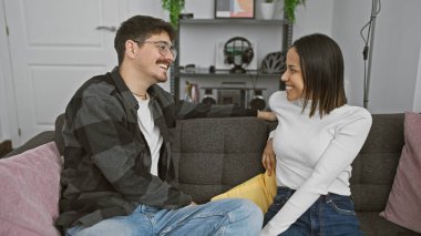 Mutlu çift, rahat, modern bir oturma odasında kanepede birlikte gülüyor.
