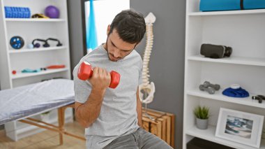 Genç bir İspanyol, rehabilitasyon kliniğinin eğitim odasında dambıllarla egzersiz yapıyor..