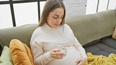 İçerde otururken su içen, sakin bir annelik hayatı tasvir eden İspanyol kadın bekleniyor..