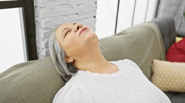 Olgun bir kadın rahat bir kanepede dinleniyor, rahat, aydınlık bir oturma odasında, huzur içinde..