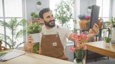 Neşeli sakallı bir adam çiçeklerle ve renkli çiçeklerle dolu parlak bir çiçekçide selfie çekiyor..