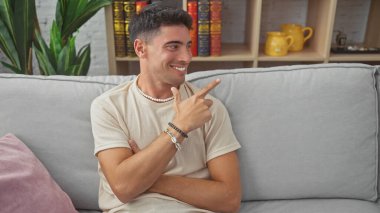 Gülümseyen İspanyol genç adam evdeki koltukta oturan, rahat, rahat ve çekici bir erkek tasvir ediyor..