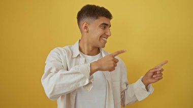 Gülümseyen adam sarı arka planda günlük kıyafetleri işaret ediyor..