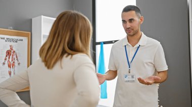 Erkek bir terapist, arka planda kas sistemi çizelgesi olan bir rehabilitasyon kliniğinde kadın bir hastayla konuşuyor..