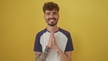 Sarı izole bir arka planda duran kendine güvenen genç bir İspanyol adam, ellerinin birliğiyle dua ediyor, af diliyor.
