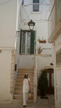 Beyaz elbiseli genç bir İspanyol kadın, İtalya, Avrupa 'daki eski Locorotondo, Puglia caddelerini beyazlatılmış binaları ve büyüleyici mimarisi ile keşfediyor..