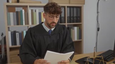 Yargıç cüppeli genç adam modern bir ofiste kitap rafları ve hukuki terazileri olan belgeler okuyor.