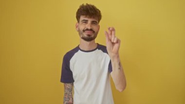İzole edilmiş sarı arka planda duran kendinden emin genç İspanyol adam gülümsüyor ve mutlu bir şekilde parmaklarıyla üç numarayı gösteriyor.