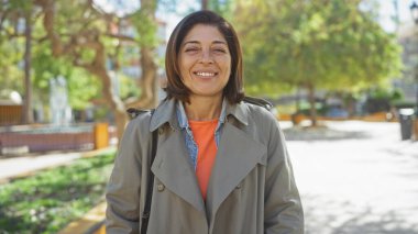 Parkta gülümseyen orta yaşlı İspanyol kadın pozitifliği ve olgunluğu resmediyor..