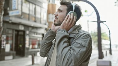 Sakallı genç bir İspanyol, şehir sokaklarında kulaklıkla müzik dinlemekten hoşlanıyor..