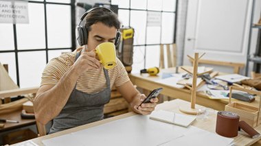 Sakallı, kahve içen ve bir marangoz atölyesinde telefonu kontrol eden İspanyol bir adam.