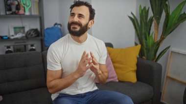 Gülümseyen sakallı bir adam modern bir oturma odasında modern bir dekorla el çırpıyor..