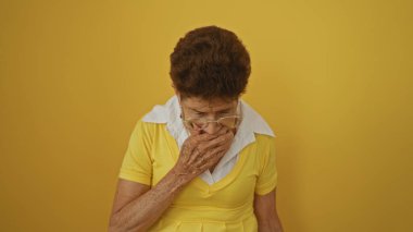 Yaşlı, İspanyol bir kadın, gözlük takıyor ve sarı bluzlu. Sarı bir duvarın karşısında duruyor. Derin düşüncelere dalmış ve ciddi görünüyor..