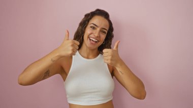 Çekici genç Latin esmer kadın gülümsüyor ve pembe arka plandan izole bir şekilde başparmak kaldırıyor.