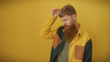 Sarışın, sakallı, kızıl saçlı bir adam sarı arka planda poz veriyor..