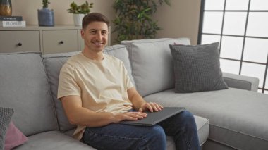 Modern bir oturma odasındaki rahat bir kanepede otururken içeride gülümseyen yakışıklı bir genç adam..