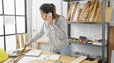 Ahşap atölyesinde ahşap, ahşap ve güvenlik teçhizatlarıyla İspanyol kadın telefonda.