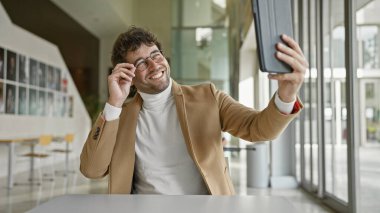 Gülümseyen İspanyol adam modern ofiste gözlük ve günlük kıyafetlerle selfie çekiyor..
