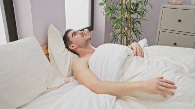 Yakışıklı İspanyol bir adam beyaz bir yatak odasında düşünceli bir şekilde yatıyor..