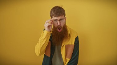 Gözlüklü, sarı arka planda renkli gömlekli, sakallı, şaşırmış bir genç..